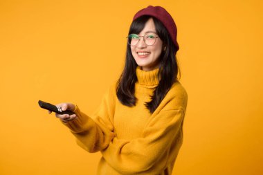 Sarı kazaklı, uzaktan kumandalı ve televizyon izleyen mutlu genç bir kadının olduğu rahat bir ev sahnesi..