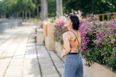 Şehir gün batımında turuncu gömlekli mutlu bir kadın şehir yolunda yürüyor..