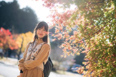 Şık giyinen Asyalı kadın, Kyoto 'nun sonbahar güzelliğini keşfediyor. Japon geleneğinin canlı yeşillikleri ve manzaralı cazibesi arasında neşeli gülümsemeler yakalıyor..