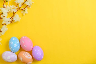 Mutlu Paskalya bayramı tebrik kartı konsepti. Sarı arka planda renkli Paskalya yumurtaları ve bahar çiçekleri. Üst görünüm, düz görünüm, kopyalama alanı.