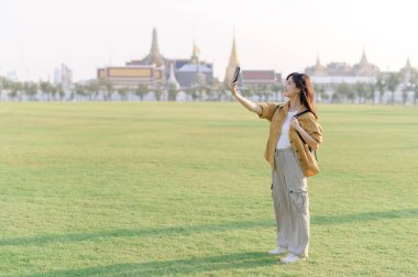 Gezgin Asyalı 30 'lu yaşlardaki kadın Wat Phra Kaew zümrüt Buda' yı keşfederken akıllı telefondan canlı yayın yapıyor. Yolculuğu boyunca Tayland mirasının mucizelerini paylaş..