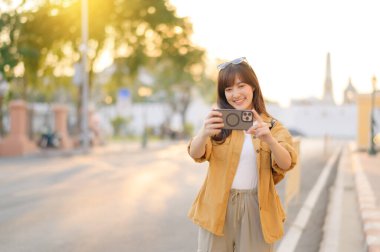 Gezgin Asyalı 30 'lu yaşlarda bir kadın Bangkok, Tayland' da şehir caddesinde dolaşırken fotoğraf çekmek için akıllı telefon kullanıyor.