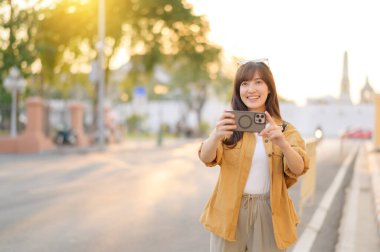 Gezgin Asyalı 30 'lu yaşlarda bir kadın Bangkok, Tayland' da şehir caddesinde dolaşırken fotoğraf çekmek için akıllı telefon kullanıyor.