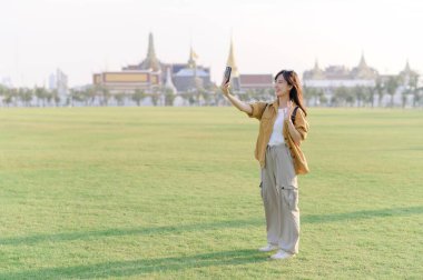 Gezgin Asyalı 30 'lu yaşlardaki kadın Wat Phra Kaew zümrüt Buda' yı keşfederken akıllı telefondan canlı yayın yapıyor. Yolculuğu boyunca Tayland mirasının mucizelerini paylaş..