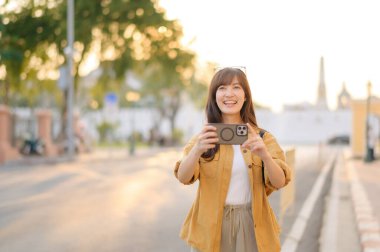 Gezgin Asyalı 30 'lu yaşlarda bir kadın Bangkok, Tayland' da şehir caddesinde dolaşırken fotoğraf çekmek için akıllı telefon kullanıyor.