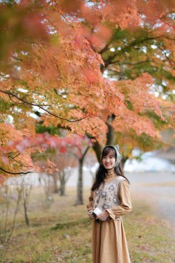 Gündelik elbiseli Asyalı kadın, gülümseme, moda ve canlı yeşilliklerle dolu bir bayramın tadını çıkararak Japonya 'nın güzelliğini kucaklıyor. Tatilin özünü yansıtan neşeli bir portre..