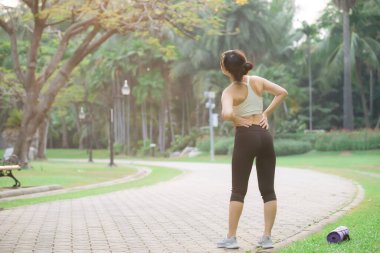Sırt ağrısı sorunu. Kadın koşucu. 30 'lu yaşlarda beyaz spor giysili Asyalı bir kadın parkta koştuktan sonra acıdan sırtüstü yatıyor..