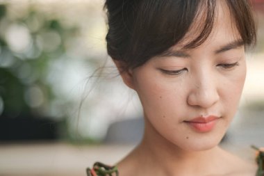 Asyalı, düşünceli, Asyalı genç bir kadın. Doğal makyajı, hafif ışıklandırması ve bulanık bir geçmişi var. Huzurlu ve iç gözlem havası yaratıyor.