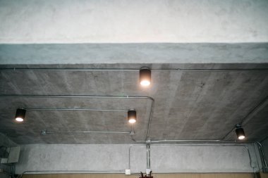 Modern tavan lambalarıyla korunmasız bir beton tavan.