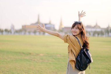 30 'lu yaşlarda, Bangkok' ta gün batımının altın parıltısıyla yıkanmış, tasasız bir sevinçle gülen, o anın özgürlüğünü kucaklar gibi kollarını açmış, gezgin bir Asyalı kadın. Sırt çantası bağlandı..