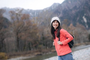 Pembe postu olan Asyalı kadın Japonya 'nın manzaralı güzelliğini keşfediyor. Göl kenarında yürüyüş, yolculuğun başarısını ve heyecanını gösteren zarif bir portre..