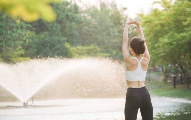 Kadın koşucu. Spor giyim kuşağı olan sağlıklı bir Asyalı kadın koşup dışarıda eğlenmeden önce parkta kaslarını esnetiyor. Kamu parkındaki spor koşucusu kız. Refah konsept demek.