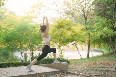 Kadın koşucu. Spor giyim kuşağı olan sağlıklı bir Asyalı kadın koşup dışarıda eğlenmeden önce parkta kaslarını esnetiyor. Kamu parkındaki spor koşucusu kız. Refah konsept demek.