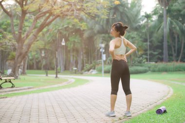 Sırt ağrısı sorunu. Kadın koşucu. 30 'lu yaşlarda beyaz spor giysili Asyalı bir kadın parkta koştuktan sonra acıdan sırtüstü yatıyor..