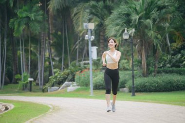 Yeşil doğa parkında koşan Asyalı kadın koşucu.