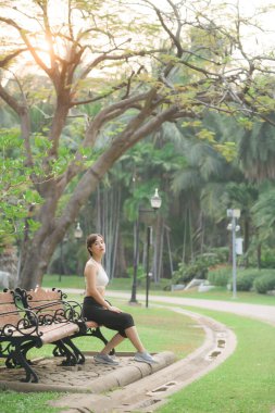 Kadın koşucu koşudan sonra dinleniyor ve bankta oturuyor.