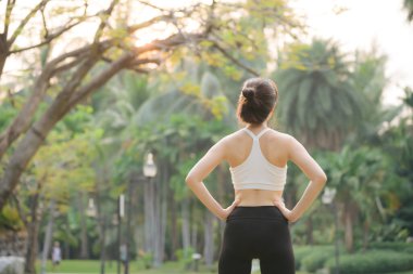 Kadın koşucu. Spor giyim kuşağı olan sağlıklı bir Asyalı kadın koşup dışarıda eğlenmeden önce parkta kaslarını esnetiyor. Kamu parkındaki spor koşucusu kız. Refah konsept demek.