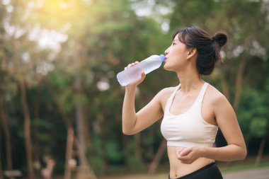 Kadın koşucu. Sağlıklı bir açık havada koşup eğlendikten sonra beyaz spor giyim suyuyla zinde bir Asyalı genç kadın. Kamu parkındaki spor koşucusu kız. Refah konsept demek.
