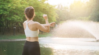 Kadın koşucu. Spor giyim kuşağı olan sağlıklı bir Asyalı kadın koşup dışarıda eğlenmeden önce parkta kaslarını esnetiyor. Kamu parkındaki spor koşucusu kız. Refah konsept demek.
