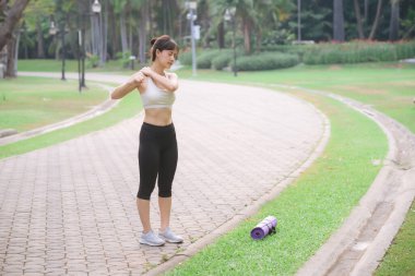 Omuz ağrısı sorunu. Kadın koşucu. 30 'lu yaşlarda beyaz spor giysili Asyalı bir kadın parkta koştuktan sonra omzunu acıyla tutuyor..