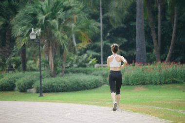 Yeşil doğa parkında koşan Asyalı kadın koşucu.