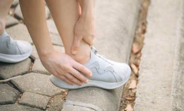 Bileği burkulmuş. Kadın koşucu. 30 'lu yaşlardaki Asyalı kadın spor giysisi giymiş parkta koştuktan sonra bileğini acıdan tutuyor..