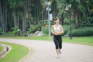 Yeşil doğa parkında koşan Asyalı kadın koşucu.
