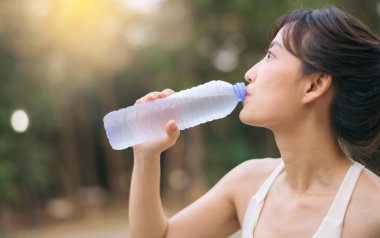 Kadın koşucu. Sağlıklı bir açık havada koşup eğlendikten sonra beyaz spor giyim suyuyla zinde bir Asyalı genç kadın. Kamu parkındaki spor koşucusu kız. Refah konsept demek.