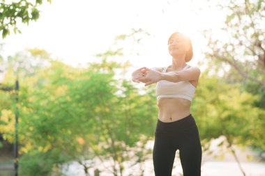 Kadın koşucu. Spor giyim kuşağı olan sağlıklı bir Asyalı kadın koşup dışarıda eğlenmeden önce parkta kaslarını esnetiyor. Kamu parkındaki spor koşucusu kız. Refah konsept demek.