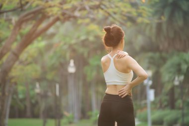 Omuz ağrısı sorunu. Kadın koşucu. 30 'lu yaşlarda beyaz spor giysili Asyalı bir kadın parkta koştuktan sonra omzunu acıyla tutuyor..