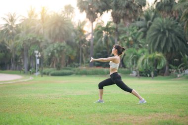 Kadın koşucu. Spor giyim kuşağı olan sağlıklı bir Asyalı kadın koşup dışarıda eğlenmeden önce parkta kaslarını esnetiyor. Kamu parkındaki spor koşucusu kız. Refah konsept demek.