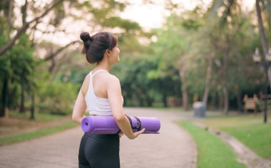 Fitness yogası yapan kadının yoga minderiyle parkta yürümesi.