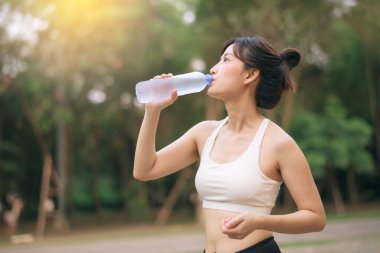Kadın koşucu. Sağlıklı bir açık havada koşup eğlendikten sonra beyaz spor giyim suyuyla zinde bir Asyalı genç kadın. Kamu parkındaki spor koşucusu kız. Refah konsept demek.