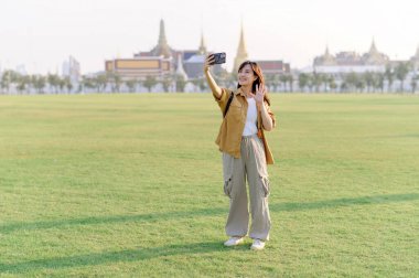 Gezgin Asyalı 30 'lu yaşlardaki kadın Wat Phra Kaew zümrüt Buda' yı keşfederken akıllı telefondan canlı yayın yapıyor. Yolculuğu boyunca Tayland mirasının mucizelerini paylaş..
