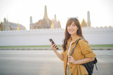 Gezgin Asyalı 30 'lu yaşlarda bir kadın Bangkok, Tayland' daki şehir caddesinde navigasyon için akıllı telefon kullanıyor..