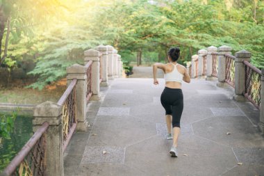 Halk parkında köprüden koşarak geçen Asyalı kadın koşucu..