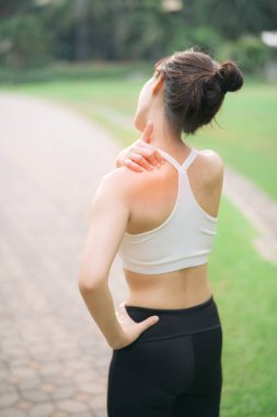 Omuz ağrısı sorunu. Kadın koşucu. 30 'lu yaşlarda beyaz spor giysili Asyalı bir kadın parkta koştuktan sonra omzunu acıyla tutuyor..