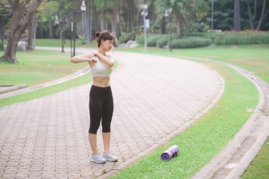 Omuz ağrısı sorunu. Kadın koşucu. 30 'lu yaşlarda beyaz spor giysili Asyalı bir kadın parkta koştuktan sonra omzunu acıyla tutuyor..