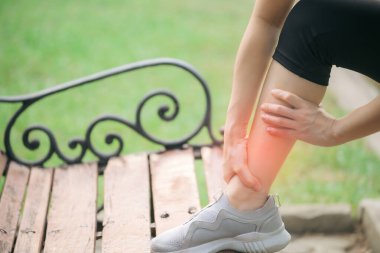 Bileği burkulmuş. Kadın koşucu. 30 'lu yaşlardaki Asyalı kadın spor giysisi giymiş parkta koştuktan sonra bileğini acıdan tutuyor..