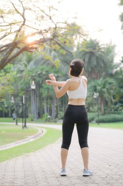 Kadın koşucu. Spor giyim kuşağı olan sağlıklı bir Asyalı kadın koşup dışarıda eğlenmeden önce parkta kaslarını esnetiyor. Kamu parkındaki spor koşucusu kız. Refah konsept demek.