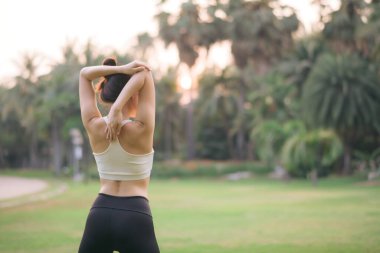 Kadın koşucu. Spor giyim kuşağı olan sağlıklı bir Asyalı kadın koşup dışarıda eğlenmeden önce parkta kaslarını esnetiyor. Kamu parkındaki spor koşucusu kız. Refah konsept demek.