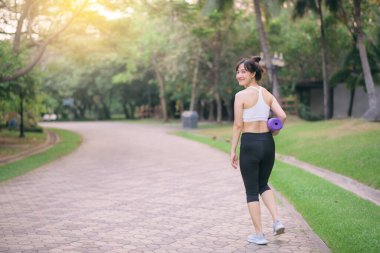 Yoga minderiyle parkta yürüyen güzel bir fitness yoga kadını.