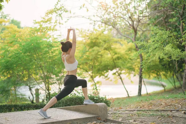 Kadın koşucu. Spor giyim kuşağı olan sağlıklı bir Asyalı kadın koşup dışarıda eğlenmeden önce parkta kaslarını esnetiyor. Kamu parkındaki spor koşucusu kız. Refah konsept demek.