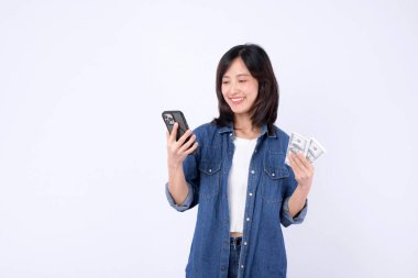 Güneydoğu Asyalı kadın cep telefonu kullanırken gülümsüyor ve günlük kot kıyafetleriyle internet uygulaması ile para tutuyor.