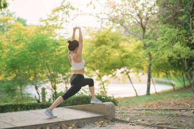 Güneydoğu Asyalı kadın yeşil ağaçlarla çevrili huzurlu parkta egzersiz yaparak sağlık ve sağlıklı yaşam tarzı kavramı uyguluyor.