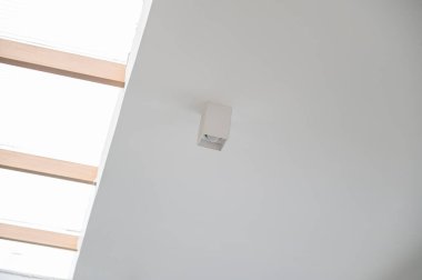 Ahşap kirişlerden gelen doğal ışık ile temiz beyaz tavana monte edilmiş minimalist bir tavan lambası modern ve parlak bir iç atmosfer yaratıyor.