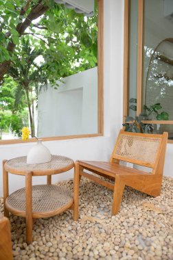 İçinde ahşap sandalye ve vazo ve yeşil ağaçların gölgesi altında çakıl taşlarıyla çevrili sarı çiçekli yuvarlak bir masa olan rahat bir açık hava oturma alanı. Rahatlamak için mükemmel.