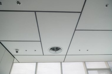 Temiz, modern bir ofis tavanı. Havalandırma delikleri, tenha aydınlatma ve beyaz paneller ve minimalist tasarım ile ızgara deseni parlak ve düzenli bir atmosfer yaratıyor.