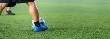 Yeşil çimlerin üzerinde hareket eden bir futbolcu maç sırasında bacaklarına ve toplarına odaklanıyor, hareketlerini ve spor enerjilerini yakından gösteriyor