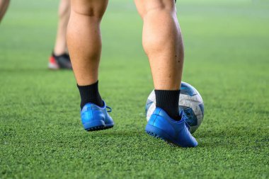 Futbol oyuncuları çim sahada hareket halindeyken bacaklarına ve toplarına odaklanırlar. Mavi kramponlar ve siyah çoraplar hareket halindedir. Arka plan bulanıktır.